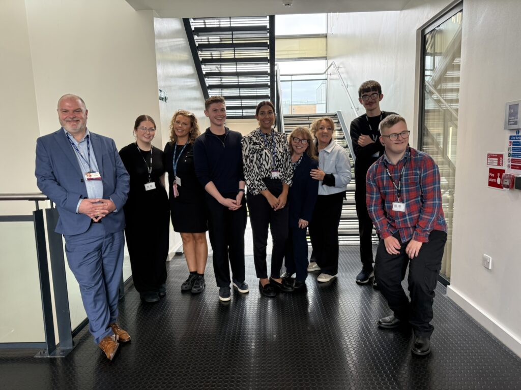 Group of nine people posing together in a hallway near a staircase
