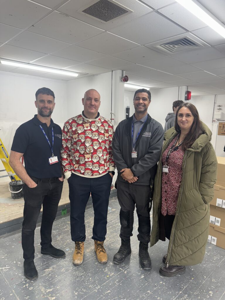 Four people standing together in an indoor workshop.